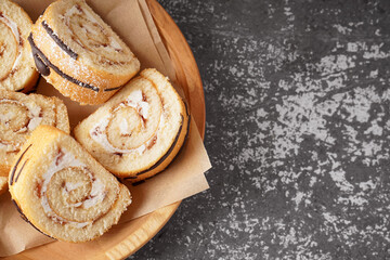 Wooden plate with pieces of delicious sponge cake roll on grey table