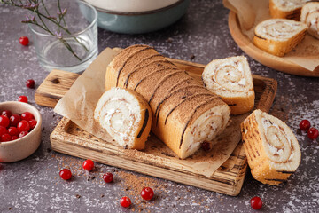 Cutting board with delicious sponge cake roll and fresh cranberries on grey table