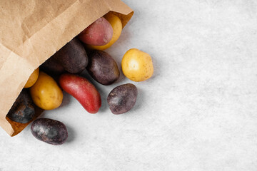 Paper bag with different raw potatoes on light background