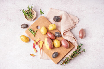 Wooden board with different raw potatoes and fresh herbs on light background