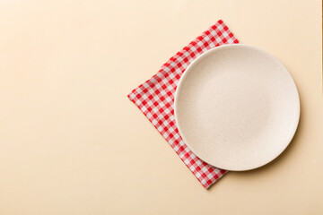 Top view on colored background empty round white plate on tablecloth for food. Empty dish on napkin...