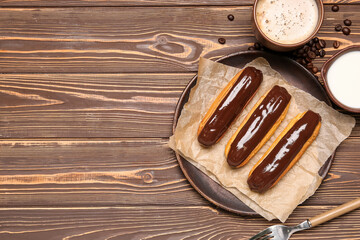 Plate with chocolate eclairs, cup of coffee and milk on wooden background