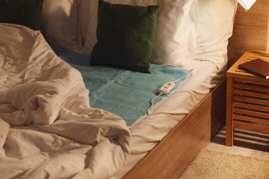Bed with electric heating pad in bedroom at night