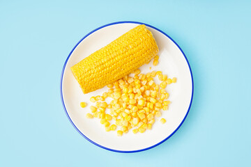 Plate with corn cob and kernels on blue background