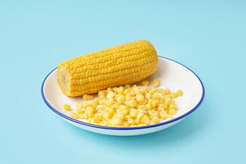 Plate with corn cob and kernels on blue background