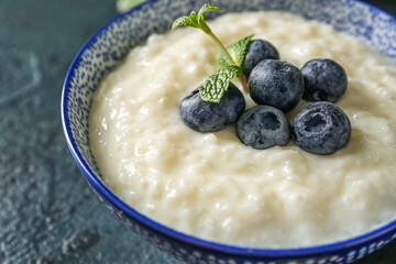 Bowl with delicious rice pudding and blueberries on black background