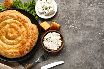 Plate with delicious cheese pie, lettuce and ingredients on grey table
