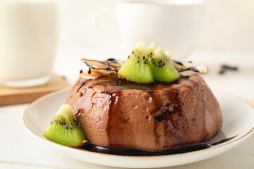 Plate with delicious pudding, chocolate sauce, kiwi and coconut slices on white table