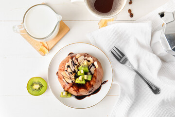 Plate with delicious pudding, chocolate sauce, kiwi, coconut, glass of milk and coffee on white table