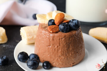 Plate with delicious chocolate pudding, almonds, blueberry and banana on black table
