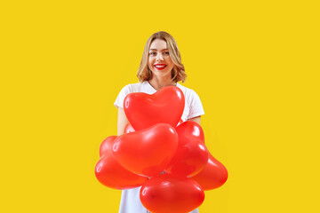 Beautiful young woman with red heart-shaped balloons on yellow background