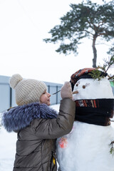 A child paints a snowman's face with paints - winter entertainment and creativity, sculpting a snowman in winter outdoor.