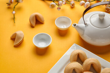 Fortune cookies, teapot, cups and sakura on yellow background. Chinese New Year celebration