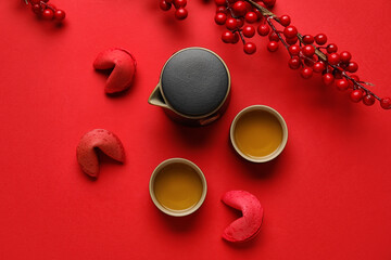 Fortune cookies, teapot, cups of tea and berries on red background. Chinese New Year celebration