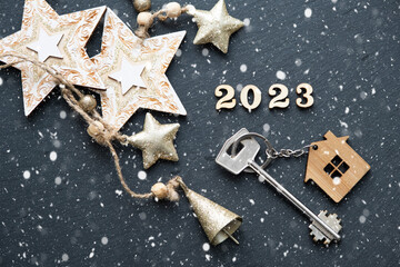 House key with keychain cottage on black background with stars, snowflakes. Happy New Year 2023-wooden letters, greeting card. Purchase, construction, relocation, mortgage