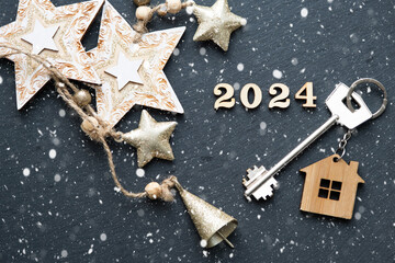 House key with keychain cottage on black background with stars, snowflakes. Happy New Year 2024-wooden letters, greeting card. Purchase, construction, relocation, mortgage
