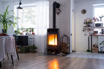 Naklejka premium Black stove, fireplace in interior of house in loft style. Alternative eco-friendly heating, warm cozy room at home, burning wood