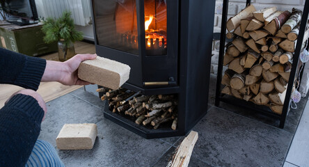 Hands kindle the hearth with economical briquettes. Fuel briquettes made of pressed sawdust for kindling the furnace - economical alternative eco-friendly fuel for the fireplace in the house. 