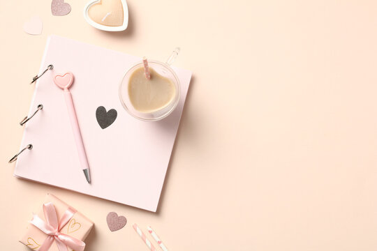 Beige desk table with pink photo album, heart shaped candles, gift boxes, cup of coffee. Valentines Day celebration concept.