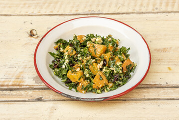 A plate with a healthy recipe for baked pumpkin salad with collard greens, raisins and fried pine nuts © Toyakisfoto.photos