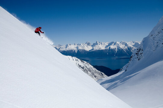Telemark skier skis down steep mountain on sunny blue sky day in Alaska backcountry.