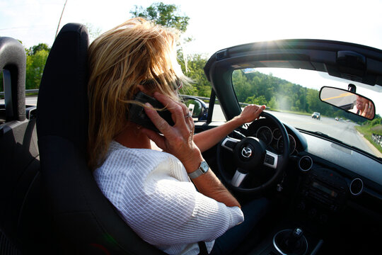 Blur-motion image of a woman driving her convertible while talking on a cell phone