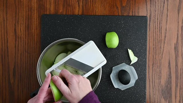 Woman&rsquo;s hands using a mandolin slicer to cut a granny smith apple into thin slices, slow motion
