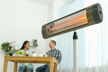 Couple spending time in room with modern electric infrared heater, focus on appliance