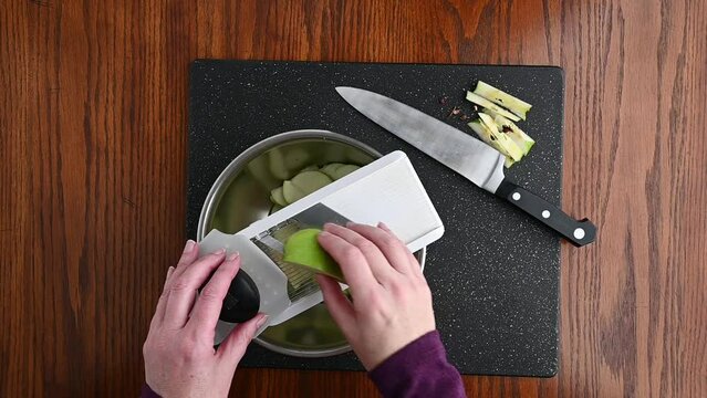 Woman&rsquo;s hands using a mandolin slicer to cut a granny smith apple into thin slices, slow motion
