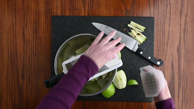 Woman&rsquo;s hands using a mandolin slicer to cut a granny smith apple into thin slices
