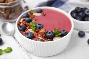 Bowl of delicious smoothie,served with fresh blueberries and granola on white tiled table, closeup