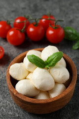 Delicious mozzarella balls in wooden bowl and basil leaves on light gray table, closeup