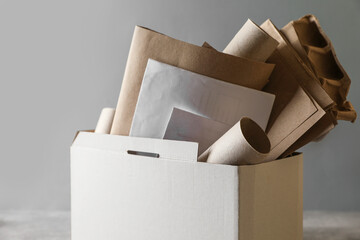 Box with different waste paper on grey table, closeup