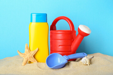 Suntan product, starfish and plastic beach toys on sand against light blue background