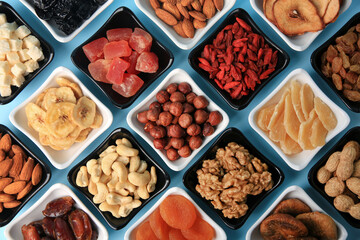Bowls with dried fruits and nuts on light blue background, flat lay