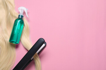 Spray bottle with thermal protection, iron and lock of blonde hair on pink background, flat lay. Space for text