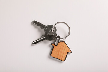 Keys with trinket in shape of house on white background, top view. Real estate agent services