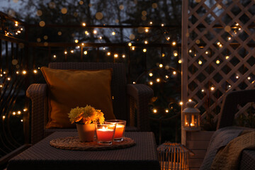 Beautiful view of garden furniture with pillow, soft blanket and burning candles at balcony