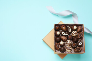 Open box of delicious chocolate candies on light blue background, flat lay. Space for text
