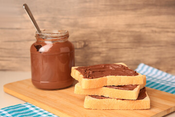 Tasty toasts with chocolate paste and jar of cream on beige table