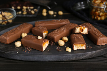 Board with delicious chocolate bars and nuts on black wooden table, closeup