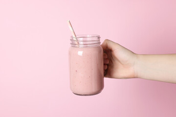 Woman holding mason jar of tasty smoothie on pink background, closeup