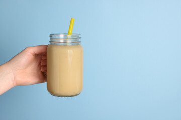 Woman holding mason jar with tasty smoothie and straw on light blue background, closeup. Space for text