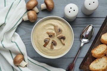 Delicious mushroom cream soup served on light grey wooden table, flat lay