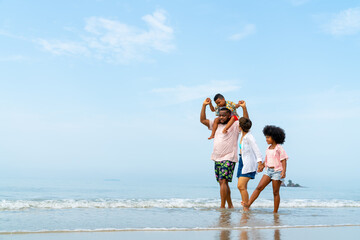  African family on summer beach holiday vacation. Father and mother with little daughter and son playing together on the beach in sunny day. Parents and kid enjoy outdoor lifestyle together at the sea