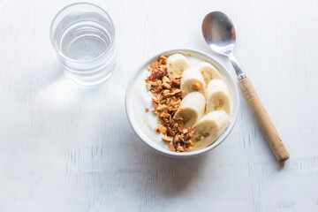 Healthy food yoghurt in bowl has banana almonds on white wood table.