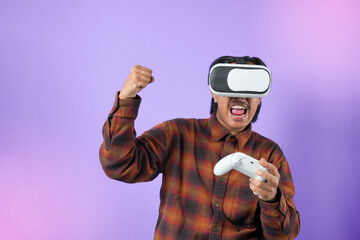 Expression of amazed asian man in VR glasses playing video game, using simulator, yelling emotionally, being excited of gaming. Indoor studio shot isolated on purple light background.