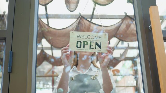 Caucasian waitress turning "welcome we are open" sign at coffeehouse.