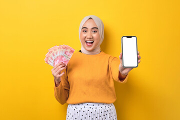 Beautiful amazed Asian girl wearing hijab showing mobile phone with blank white screen, holding...