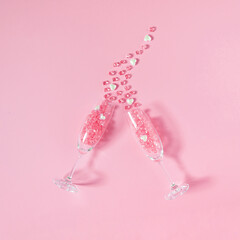 Creative composition made of two champagne glasses with pink crystal stones and white pearl hearts over pink background. Minimal Valentines Day concept or love. Top view, copy space.